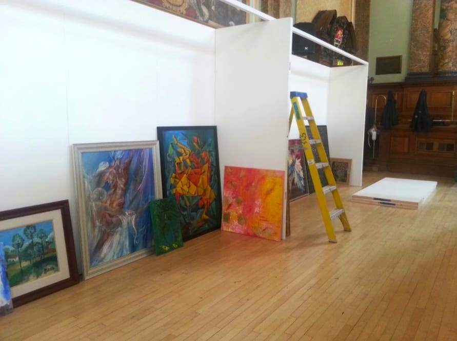 Paintings leaning against the new exhibition walls, a ladder among them, waiting to be hung.