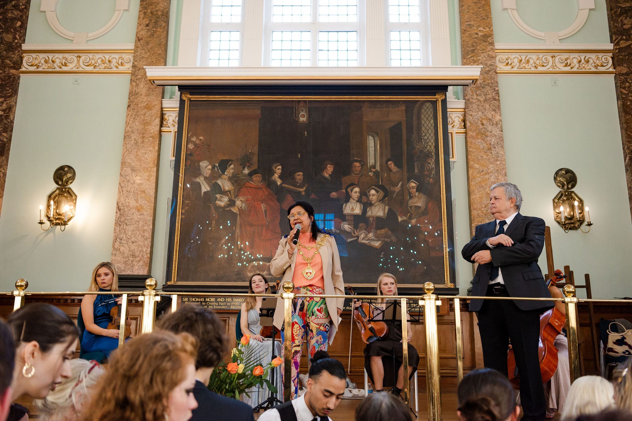 The Mayor of Kensington and Chelsea addressing a full main hall, the quartet beside her beneath the hall’s murals and gilded ceiling.