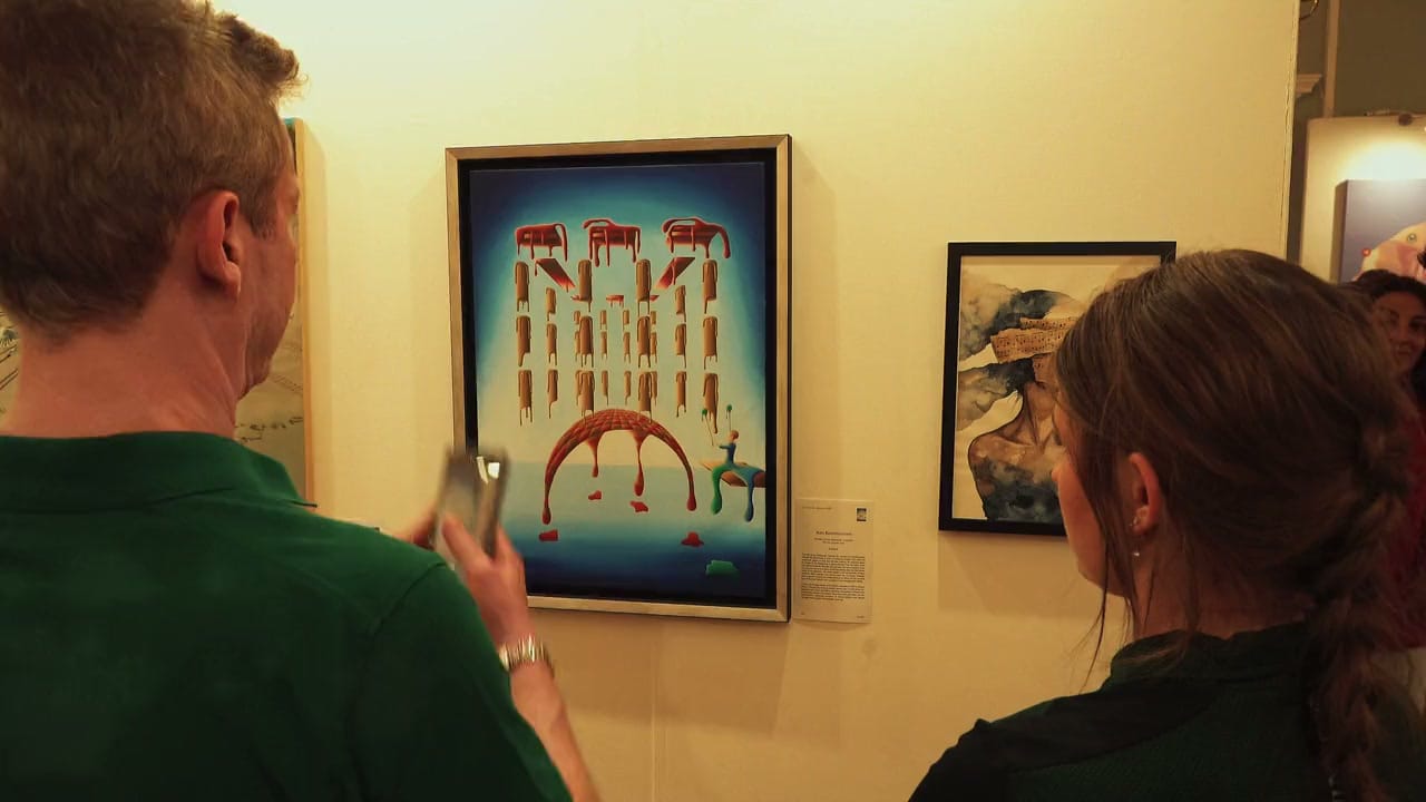 Visitors at the Seventh Edition in 2025, one photographing a surreal painting of red tables on a blue ground, hung on a white wall among other works.