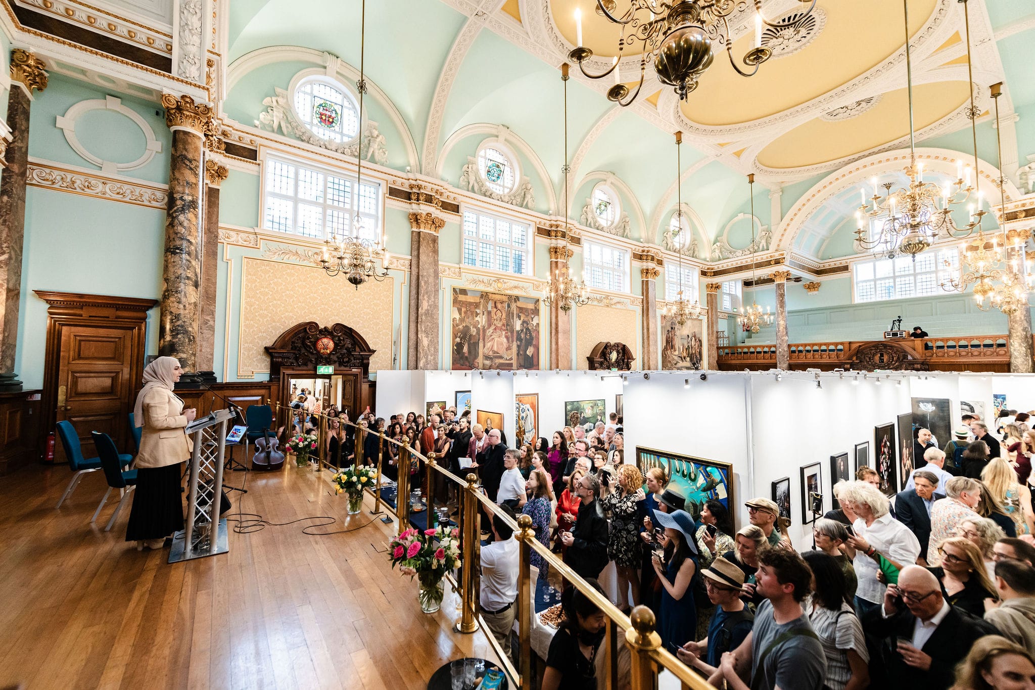 The main hall seen from the balcony during the Seventh Edition, packed with visitors beneath gilded plasterwork and chandeliers.