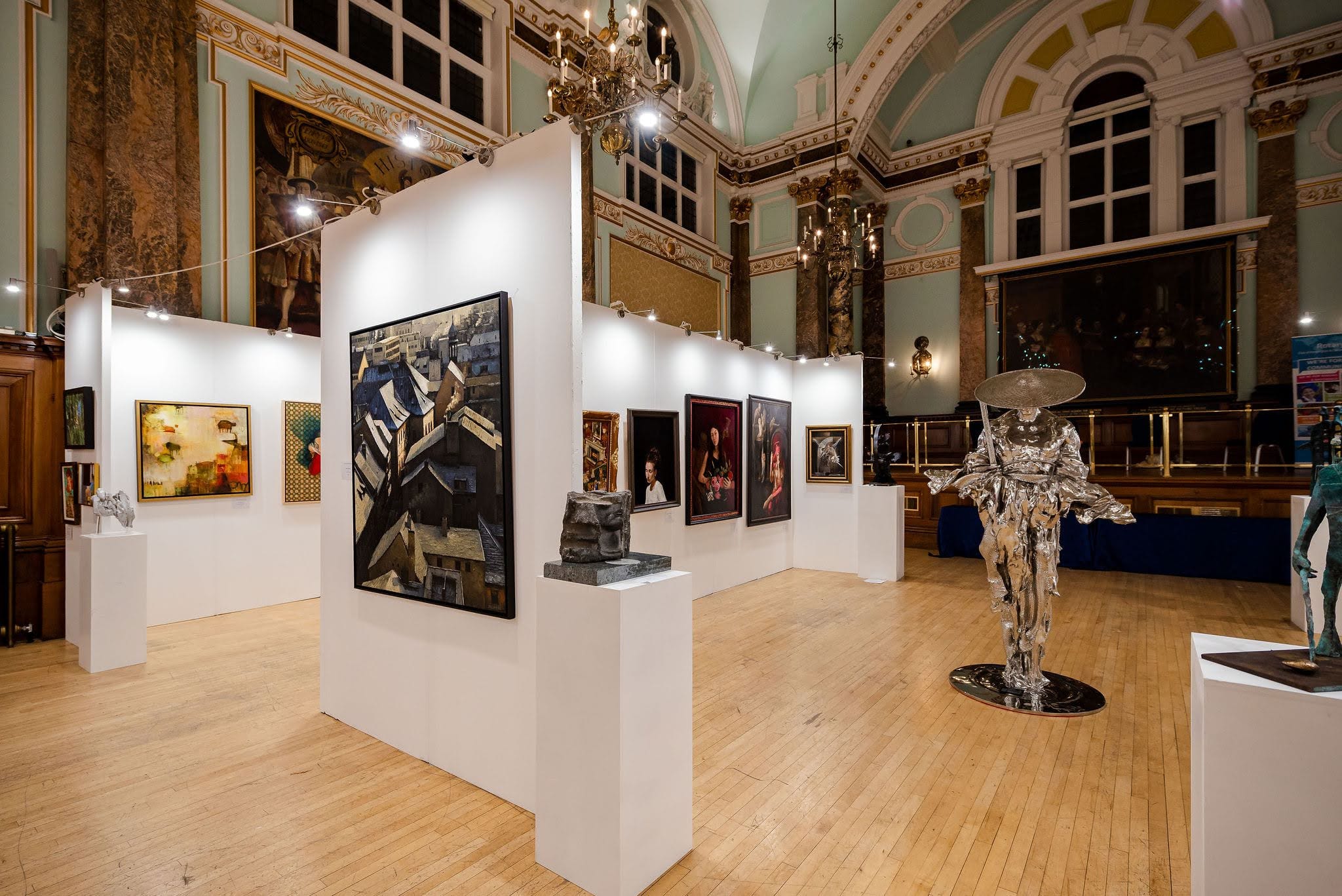 The Sixth Edition: white walls hung with paintings in the main hall, a silver figure in a wide hat standing on the parquet among them.