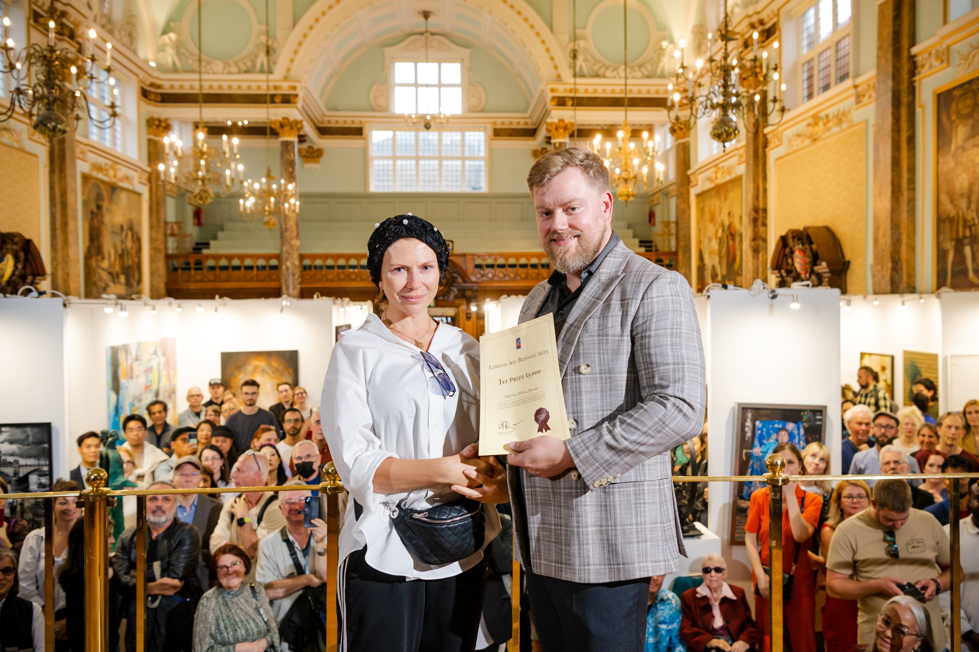 A prize winner holding up her certificate at the 2023 awards, the crowd packed behind the rail.