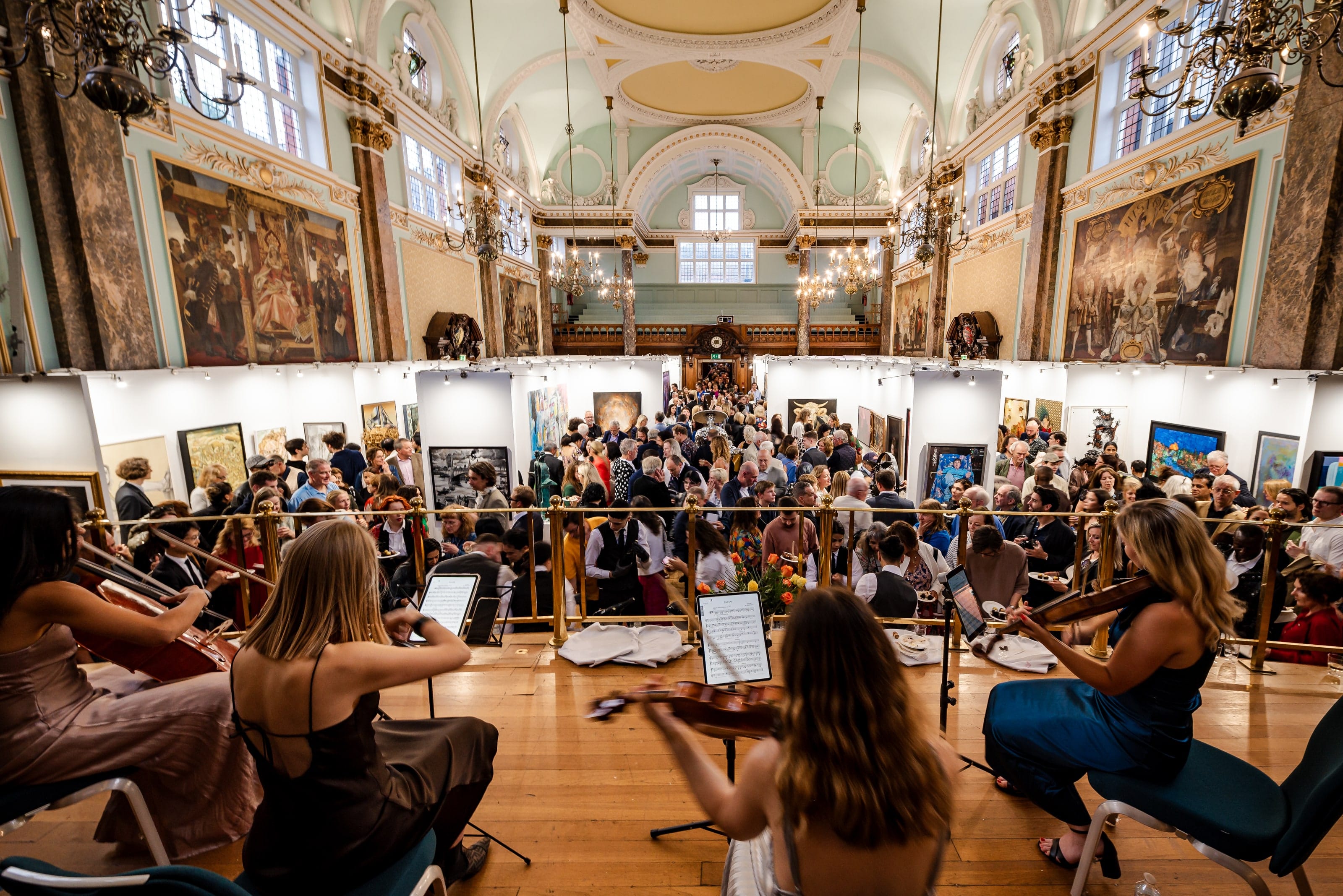 A string ensemble playing on the floor of the main hall, a crowd gathered behind them beneath the gilded vault.