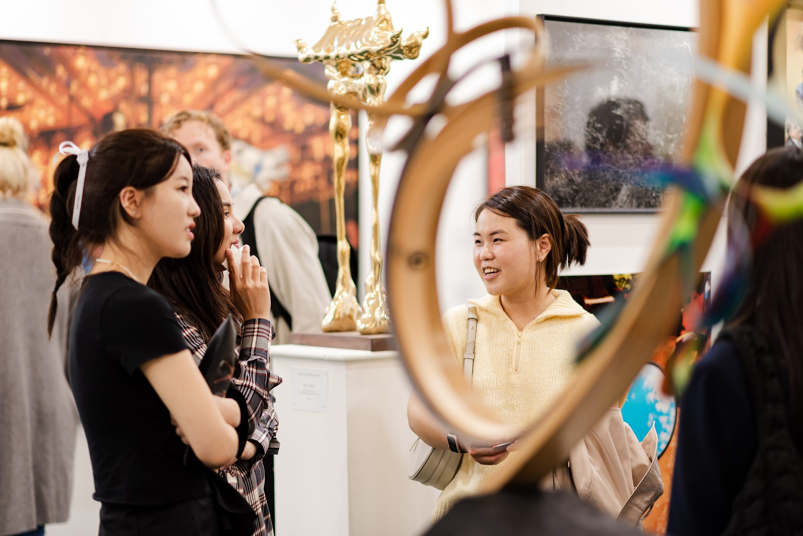 Visitors in conversation, framed through the curve of a bronze sculpture.