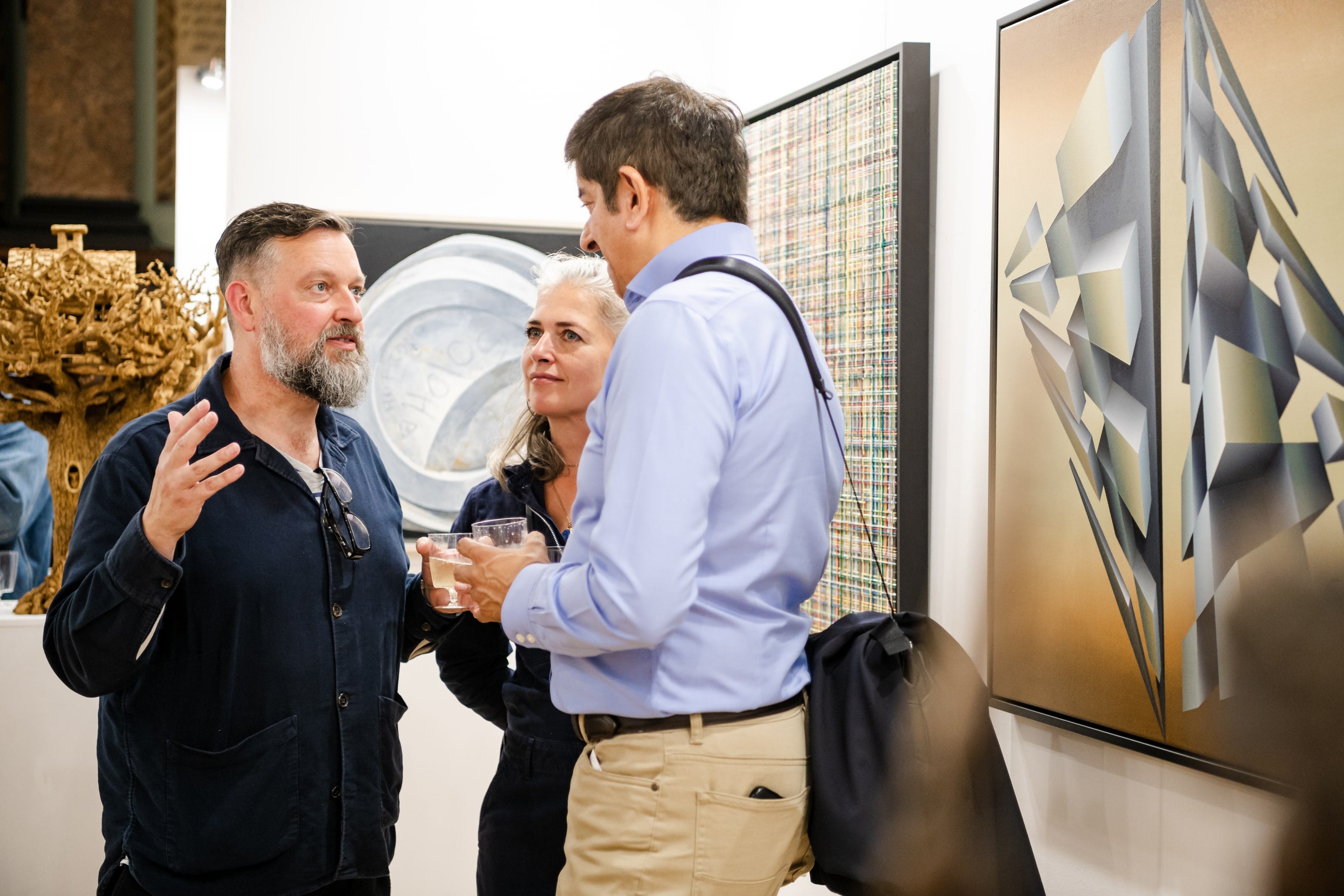 Visitors talking with drinks in hand beside large geometric paintings.